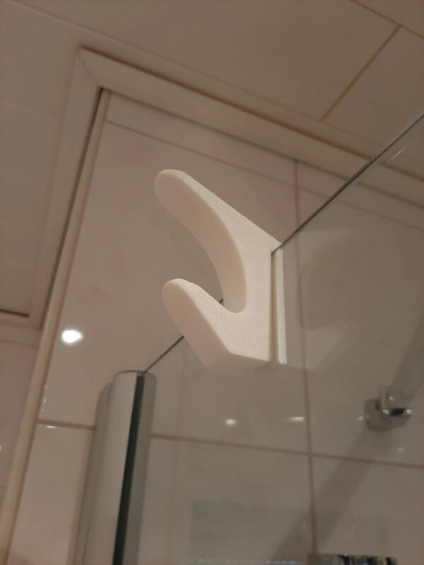Gancho doble colgando toalla en mampara de baño.